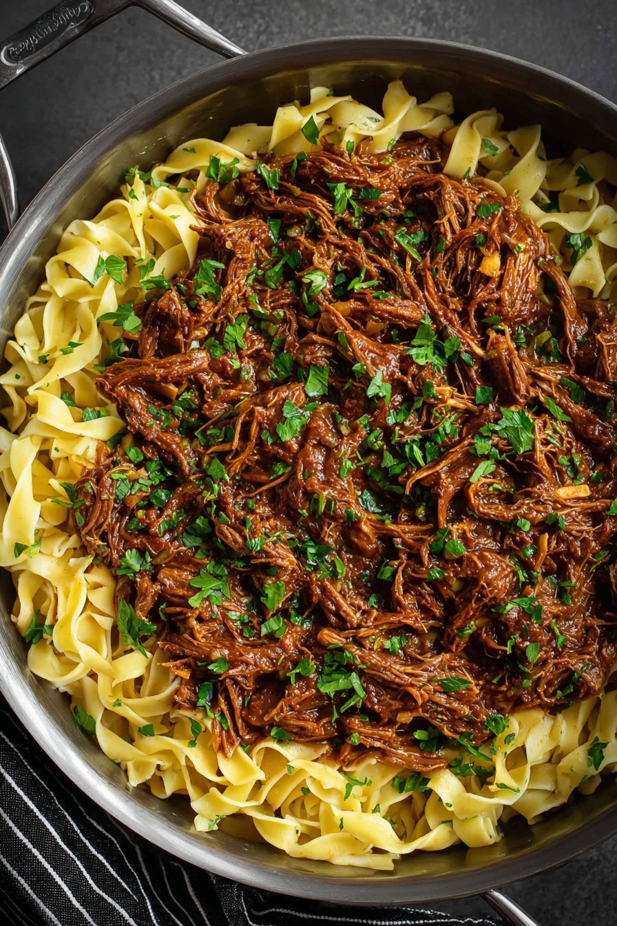 Short Rib Ragu Pasta, Braised Short Rib Pasta, Easy Short Rib Ragu, Comforting Pasta Recipes, Hearty Beef Pasta - The image shows a close-up of a pan filled with two main layers: the bottom layer is flat, wide pasta noodles in a pale yellow color, and the top layer is shredded meat cooked in a rich brown sauce. The shredded meat is mixed with small, finely chopped green herbs scattered evenly over the dish, adding spots of bright green color. The pan is metallic and round, resting on a dark gray surface with a striped black and white cloth visible at the bottom right. The overall look is hearty and rustic with a mix of smooth noodles and textured meat. photo taken with an iphone --ar 2:3 --v 7
