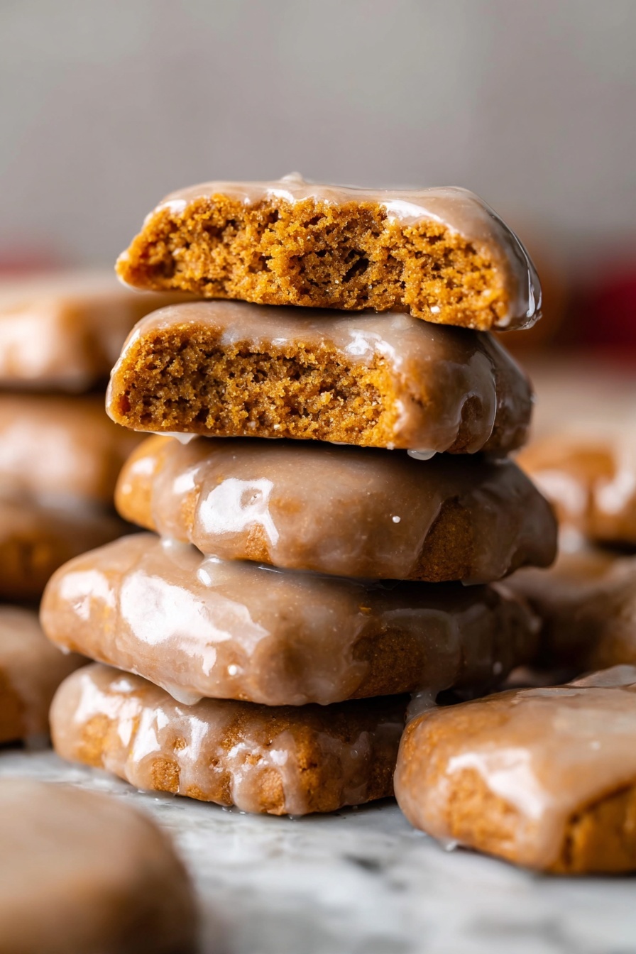 Chewy Gingerbread Man Cookies, gingerbread cookies recipe, holiday gingerbread cookies, soft gingerbread men, spiced gingerbread cookies - A stack of seven rectangular gingerbread cookies covered in a shiny light brown icing is placed on a white marbled surface. On top, one cookie is broken in half to show the soft, slightly crumbly inside, which is a warm orange-brown color. The glaze has a smooth texture with a few small spots where it drips a little around the edges. The cookies are stacked unevenly, giving a casual, fresh-baked look with more cookies softly blurred in the background. photo taken with an iphone --ar 2:3 --v 7