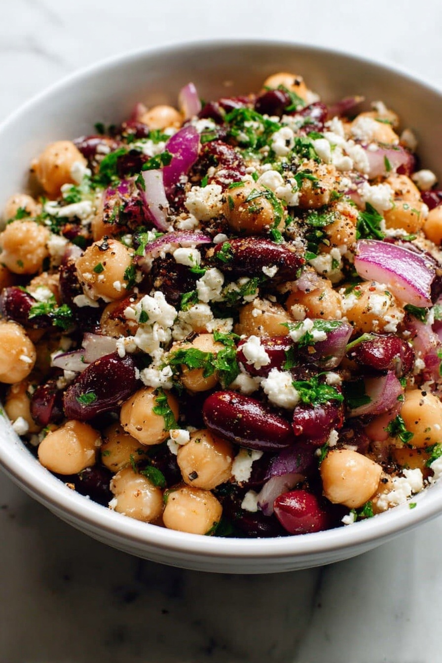 Chickpea Bean Salad with Feta, healthy chickpea salad, easy feta bean salad, vegetarian bean salad recipe, Mediterranean chickpea salad - A white bowl filled with a salad showing three main layers: the bottom layer is a mix of beige chickpeas and dark red kidney beans; the middle layer includes large pieces of purple-red onion; the top layer is sprinkled with white crumbled cheese and small bits of bright green parsley, all mixed with visible black pepper and seasoning specks. The salad looks fresh and colorful, sitting on a white marbled surface, photo taken with an iphone --ar 2:3 --v 7