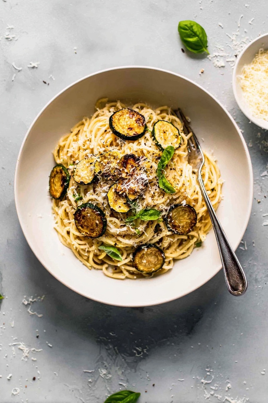 Creamy Zucchini Spaghetti, zucchini pasta with creamy sauce, healthy zucchini noodle recipe, summer vegetable pasta, easy veggie pasta dish - A white bowl filled with a mound of spaghetti pasta at the center, topped with several golden-brown, round slices of roasted zucchini scattered on and around the noodles. Small bright green basil leaves are placed over the pasta, adding a fresh touch. The spaghetti is sprinkled with finely grated white cheese, giving a light dusting over the top. A silver fork rests on the right side inside the bowl. The bowl is set on a white marbled surface with some scattered grated cheese and a few basil leaves nearby. Photo taken with an iphone --ar 2:3 --v 7