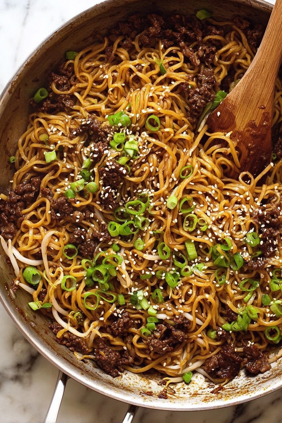 Quick Asian Beef Ramen, Asian Beef Ramen, Easy Beef Ramen, Quick Noodle Stir Fry, Flavorful Ramen Dinner - The image shows a metal pan filled with cooked noodles mixed with small pieces of dark brown meat and light bean sprouts. The noodles have a slightly shiny, brown color from the sauce. On top, there are sliced green onions and white sesame seeds scattered, adding texture and color contrast. A wooden spoon rests inside the pan, partially covered by the food. The pan sits on a white marbled surface. photo taken with an iphone --ar 2:3 --v 7