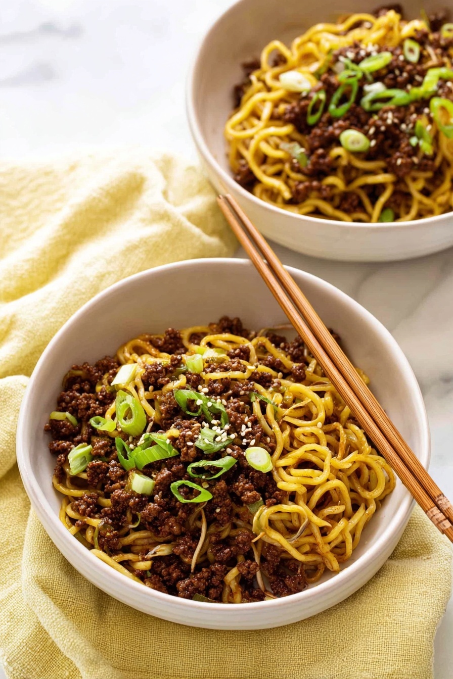 Quick Asian Beef Ramen, Asian Beef Ramen, Easy Beef Ramen, Quick Noodle Stir Fry, Flavorful Ramen Dinner - Two white bowls are filled with cooked yellow noodles mixed with dark brown ground meat and light brown bean sprouts. The noodles are topped with small, bright green chopped spring onions and a few white sesame seeds sprinkled on top. One bowl has light brown wooden chopsticks resting on its edge. The bowls sit on a soft, light yellow cloth, placed on a white marbled surface. photo taken with an iphone --ar 2:3 --v 7