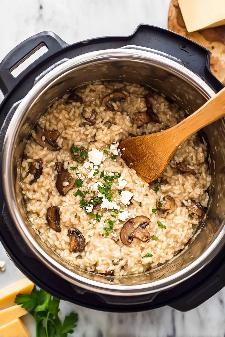 Pressure Cooker Mushroom Risotto, creamy mushroom risotto, easy pressure cooker risotto, quick mushroom risotto, hearty mushroom risotto - The image shows a close-up of a mushroom risotto inside a shiny stainless steel pot of a kitchen pressure cooker. The risotto is creamy with light beige rice mixed with pieces of cooked brown mushrooms spread evenly throughout. Some small bits of chopped green herbs and crumbled white cheese are sprinkled on top, giving a fresh and textured look. A light brown wooden spoon rests inside the risotto, leaning against the side of the pot. The pot sits on a white marbled surface, with blurred green leaves and chunks of yellow cheese in the background. Photo taken with an iphone --ar 2:3 --v 7
