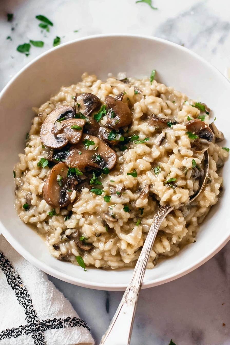 Pressure Cooker Mushroom Risotto, creamy mushroom risotto, easy pressure cooker risotto, quick mushroom risotto, hearty mushroom risotto - A white bowl filled with creamy mushroom risotto. The risotto has a thick, soft texture with plump, tender rice grains mixed with sliced brown mushrooms. Small pieces of green herbs are sprinkled on top, adding color contrast. A silver spoon is partially dipped into the risotto, resting near the edge of the bowl. The bowl sits on a white marbled surface with part of a white and black patterned cloth visible in the background. Photo taken with an iphone --ar 2:3 --v 7