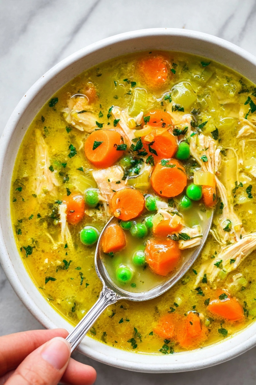 Turmeric Chicken Soup with Coconut Milk, healthy turmeric chicken soup, nourishing coconut milk soup, spicy turmeric chicken broth, easy chicken and turmeric soup - The image shows a white bowl filled with a colorful chicken soup. The soup has a yellowish broth with small pieces of shredded chicken scattered throughout. Bright orange carrot slices and vibrant green peas float on the surface along with translucent chunks of celery. Small green herb bits are sprinkled all over, adding texture and color. A silver spoon with detailing on the handle is partially submerged in the soup, held by a woman's hand, scooping some of the ingredients. The bowl sits on a white marbled surface, giving a clean and fresh look. photo taken with an iphone --ar 2:3 --v 7