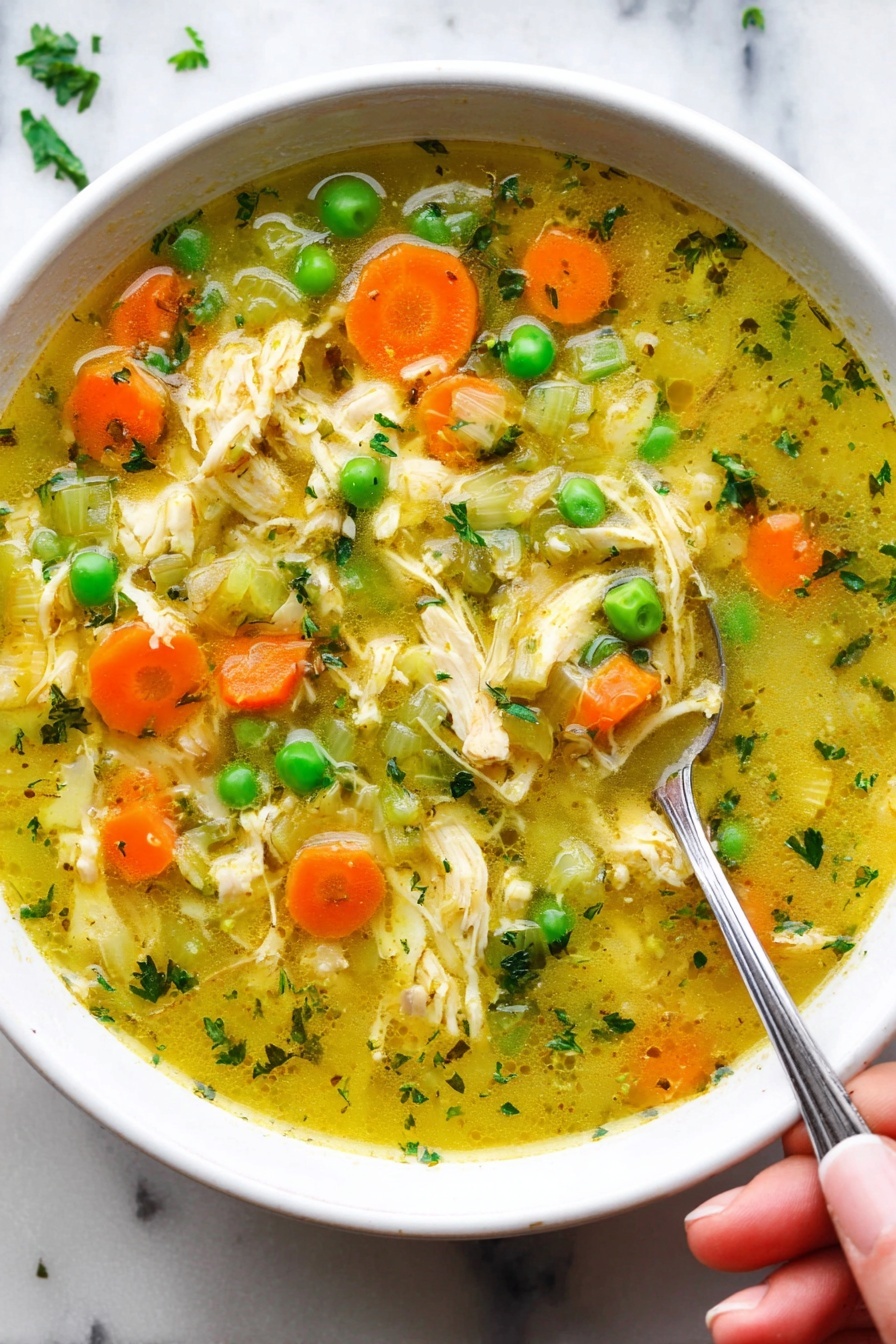 Turmeric Chicken Soup, healthy turmeric soup, nourishing chicken soup, golden turmeric chicken bowl, easy turmeric soup recipe - A close-up view of a white bowl filled with chicken soup. The soup has many layers: on top are bright orange carrot slices, green peas, and pale green celery pieces mixed with shredded light yellow chicken. The broth is clear with a yellow tint and small green herb bits floating throughout. There is a silver spoon resting in the soup, with a woman's hand holding the spoon near the edge of the bowl. The bowl is placed on a white marbled surface. Photo taken with an iphone --ar 2:3 --v 7