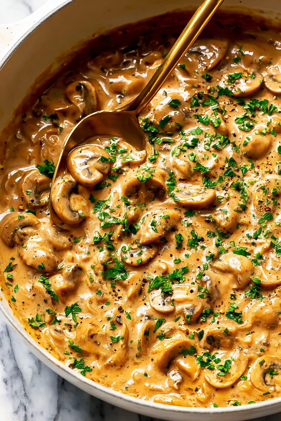 French Onion Pasta with Melted Gruyere, French Onion Pasta, cheesy pasta with caramelized onions, creamy Gruyere pasta, French-inspired pasta dish - The image shows a close-up of a white pan filled with creamy mushroom sauce. The sauce has many small round and sliced mushrooms in a thick, light brown sauce with visible black pepper and small bits of herbs. The top layer is sprinkled with fresh green chopped parsley. A brass-colored spoon is partially dipped in the sauce toward the left side of the pan. The pan is placed on a white marbled surface. Photo taken with an iphone --ar 2:3 --v 7