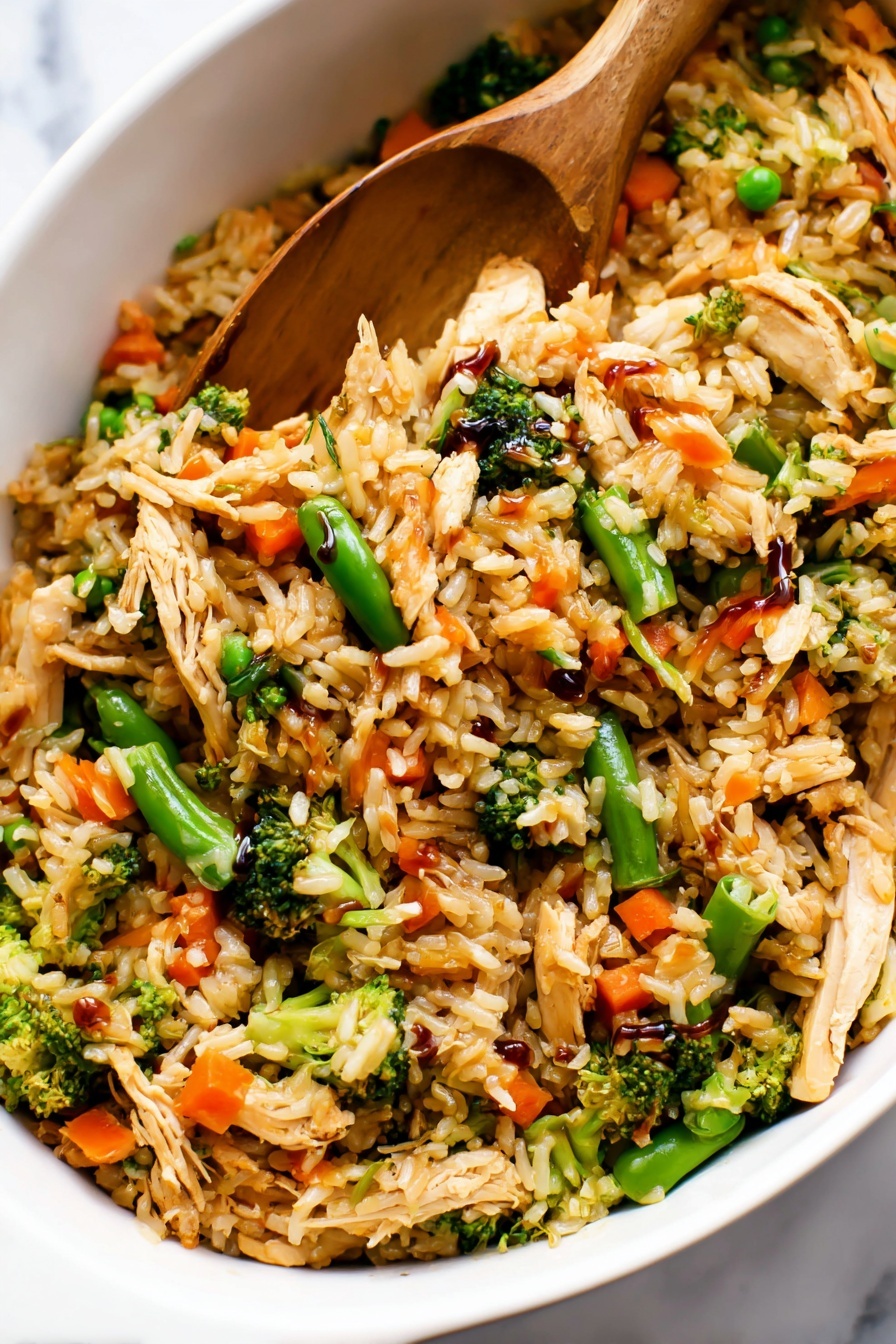 Teriyaki Chicken Casserole, easy chicken casserole recipes, weeknight dinner ideas, homemade teriyaki sauce, delicious chicken bake - The image shows a close-up of a white dish filled with a colorful fried rice mix. The dish has multiple layers: the base layer is golden-brown cooked rice, mixed with small pieces of shredded light brown cooked chicken. Scattered throughout are bright green broccoli florets and snap peas, as well as vibrant orange baby carrots. The vegetables add texture and color contrast, while some parts of the rice have a glossy look from a dark soy sauce drizzled on top. A wooden spatula is partially buried in the mixture, lifting some of the rice and vegetables. The dish is placed on a white marbled surface. Photo taken with an iphone --ar 2:3 --v 7