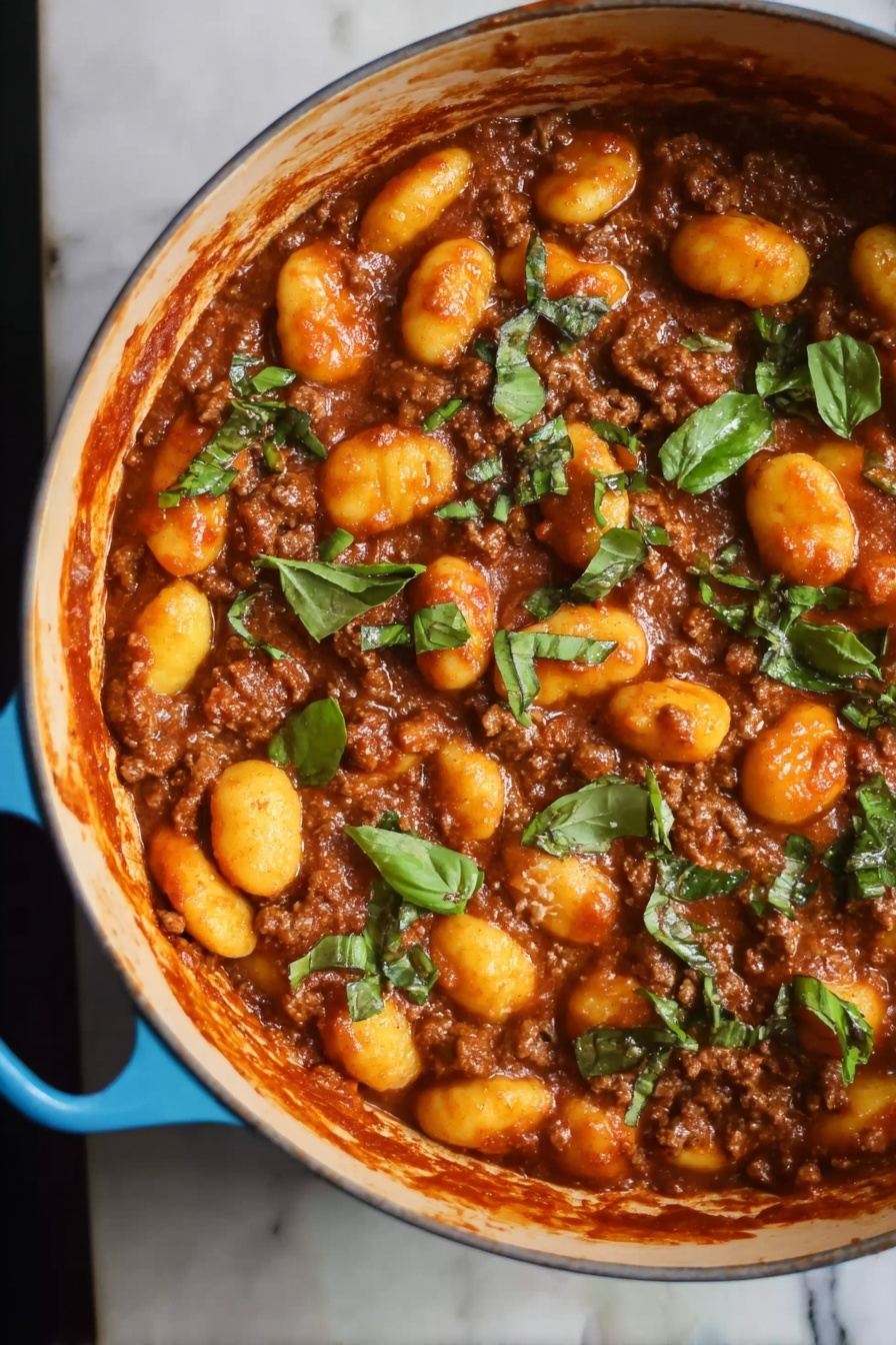 Gnocchi Bolognese, Italian Gnocchi Bolognese, Homemade Gnocchi Bolognese, Easy Gnocchi with Bolognese, Classic Gnocchi Bolognese - The image shows a blue pot filled with a rich brown meat sauce mixed with soft, yellow-orange gnocchi. The top layer is scattered with pieces of fresh green herbs, adding a bright contrast to the warm colors of the sauce and gnocchi. The pot's handle is visible on the right side, resting on a white marbled surface. The texture of the gnocchi looks smooth and tender, while the meat sauce appears thick and hearty, covering all pieces evenly. Photo taken with an iphone --ar 2:3 --v 7