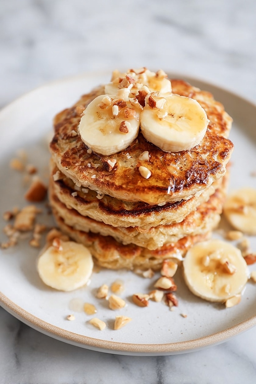 Healthy Banana Oatmeal Pancakes, healthy pancake recipes, nutritious breakfast ideas, easy oatmeal banana pancakes, gluten-free breakfast ideas - A stack of four golden-brown pancakes sits in the center of a white plate, each pancake textured with small bubbles and crispy edges. On top, there are three banana slices with a shiny drizzle of syrup pooling slightly and small pieces of chopped nuts sprinkled over them. Around the plate, scattered banana slices and nut pieces add a casual touch, all set against a white marbled background. photo taken with an iphone --ar 2:3 --v 7
