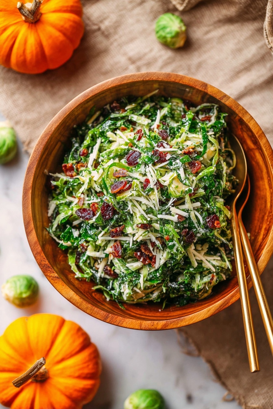 Brussels Sprout Kale Apple Salad, healthy kale and Brussels sprout salad, crunchy apple and kale salad, easy fall salad recipe, vibrant veggie salad - The image shows a wooden bowl full of a shredded green salad mixed with small bits of white cheese and dark red pieces, likely dried cranberries or bacon bits, with a texture of thin green leaves and stems. Two gold spoons rest in the bowl, positioned diagonally and partially buried in the salad. The bowl sits on a beige cloth over a white marbled surface, and in the background, bright orange small pumpkins and a few green Brussels sprouts are scattered on the same white marbled surface. The scene has a warm, natural feel with soft lighting. photo taken with an iphone --ar 2:3 --v 7