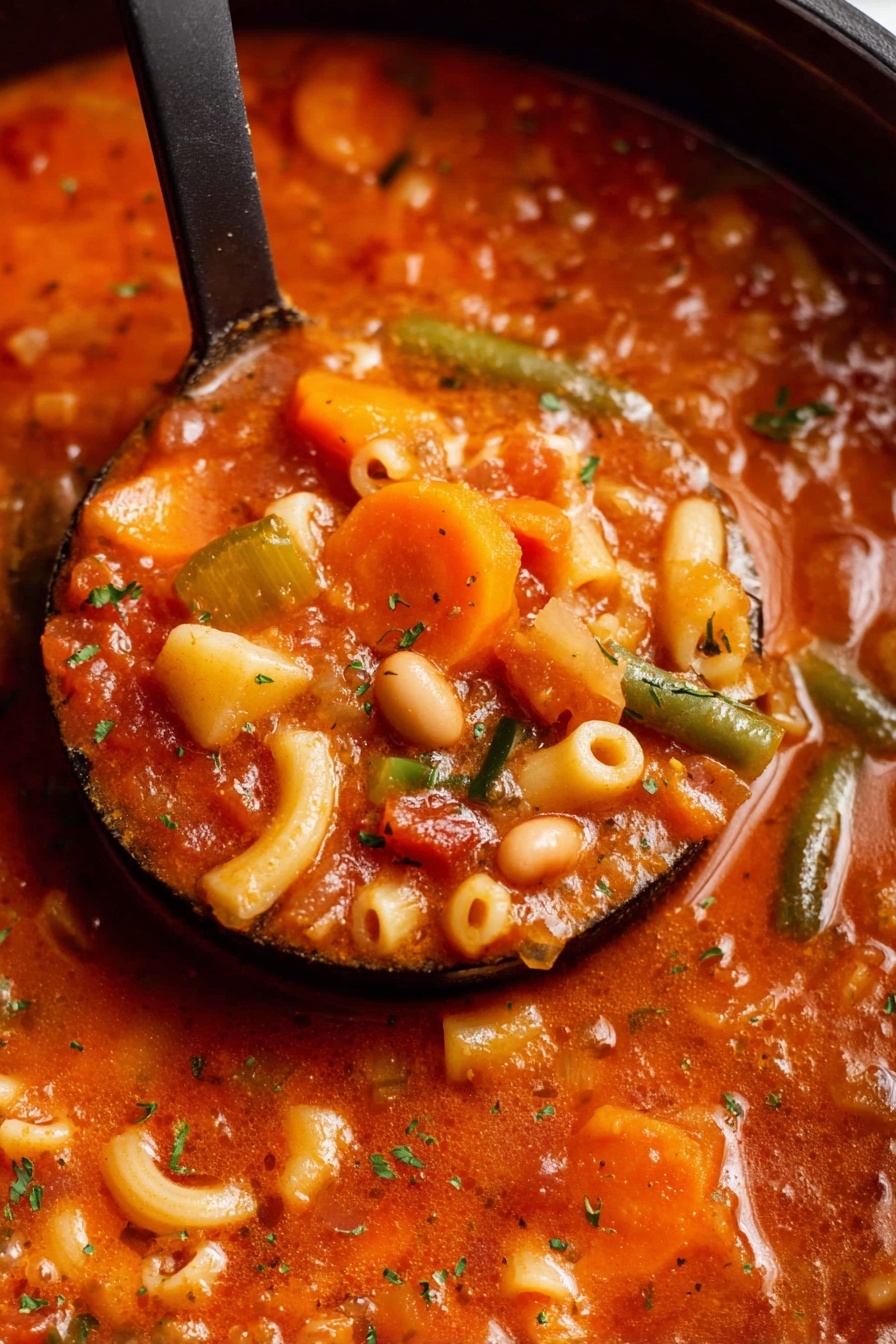 Easy Vegetarian Minestrone Soup, vegetarian minestrone soup, healthy minestrone recipe, hearty vegetable soup, quick vegetarian soup - A close-up view of a ladle full of thick vegetable soup inside a black pot, the soup has multiple layers of ingredients including orange carrot slices, white beans, small curved pasta, and bits of green beans all mixed in a rich red-orange tomato broth with specks of green herbs scattered on top, the texture looks chunky and hearty with visible soft vegetable pieces and pasta holding the soup together photo taken with an iphone --ar 2:3 --v 7