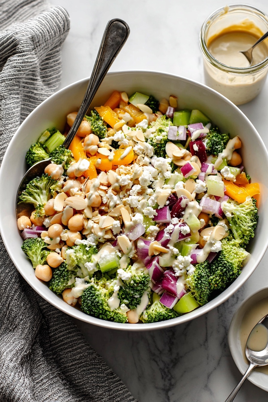Broccoli Chickpea Salad with Lemon Tahini Dressing, healthy vegan salad, quick vegetable salad, easy plant-based recipe, nutritious summer salad - A white bowl filled with a colorful salad showing multiple layers: the base layer consists of small, bright green broccoli florets and light beige chickpeas; scattered throughout are chunky orange bell pepper pieces and pale green celery bits; bright purple-red onion cubes are mixed evenly, adding contrast; white crumbled cheese pieces are sprinkled on top along with thin, light beige almond slivers; a light creamy dressing is drizzled over the salad, visible especially on the cheese and broccoli. A silver spoon rests in the bowl on the left side, and in the background there is a small glass jar with more dressing and a spoon inside it; the bowl is placed on a white marbled surface with a grey striped towel to the left. photo taken with an iphone --ar 2:3 --v 7