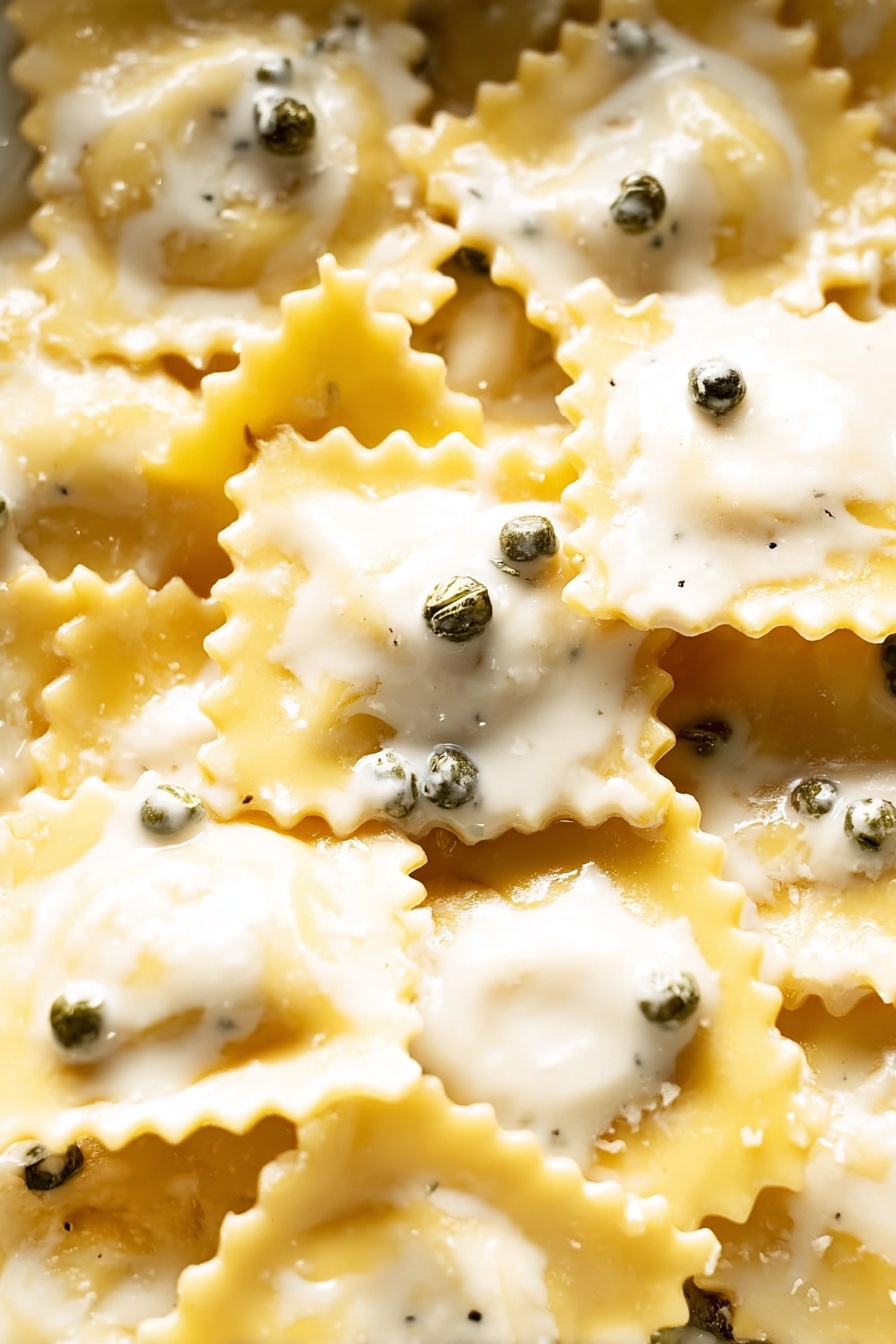 Lemon Caper Sauce for Pasta and Fish, lemon caper pasta sauce, citrus fish sauce recipe, quick lemon caper sauce, tangy seafood pasta sauce - The image shows many pieces of ravioli pasta, each piece square with scalloped edges and a pale yellow color. The ravioli are covered with a creamy white sauce that has a smooth texture and small rounded green peppercorns scattered evenly on top. The layers are mainly the ravioli base, the creamy sauce covering them, and the small green peppercorns sitting on the sauce. The image is a close-up with a soft lighting that highlights the shine and texture of the pasta and sauce, with no other objects or background visible. photo taken with an iphone --ar 2:3 --v 7